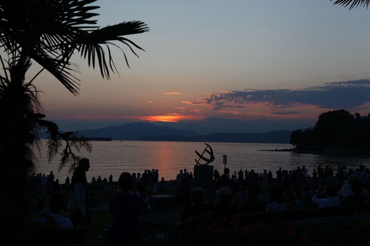 The sun setting over English Bay, silhouettes of boats and onlookers