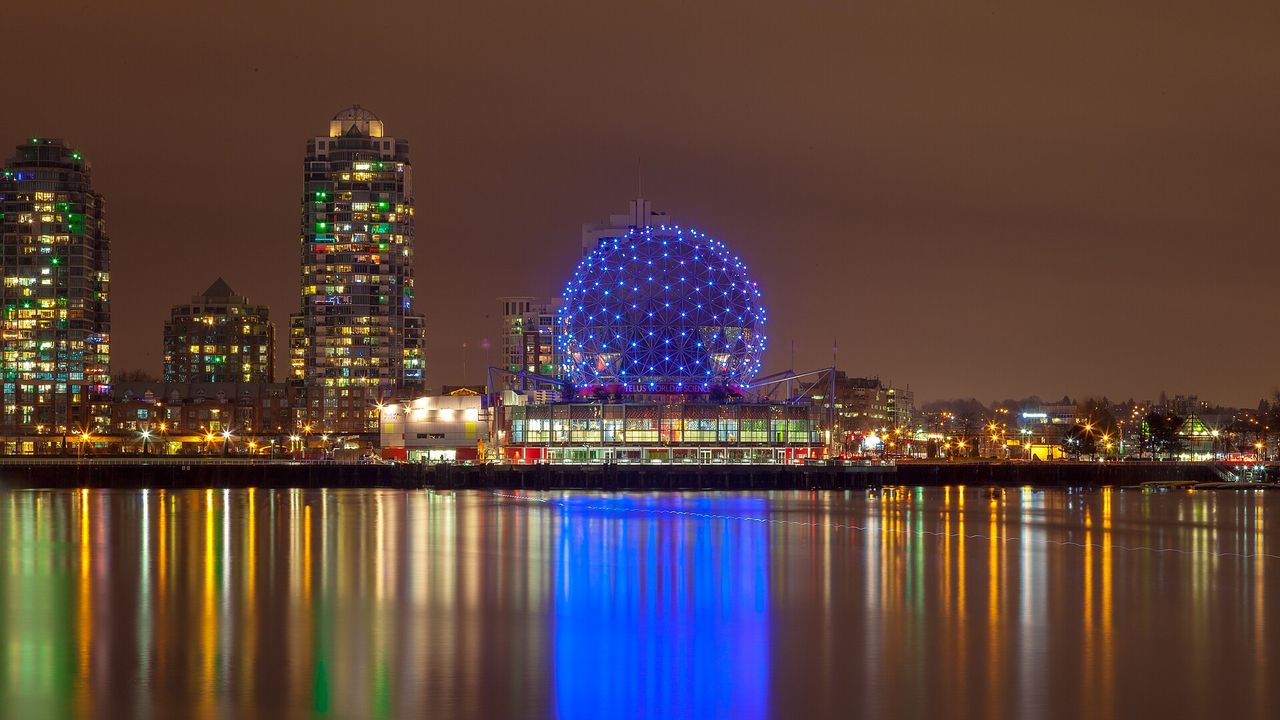Science World’s glowing geodesic dome on a rainy night, reflections on False Creek